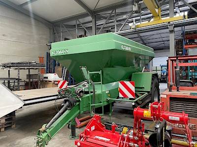 A green Kuxmann lime spreader in front view in a hangar.