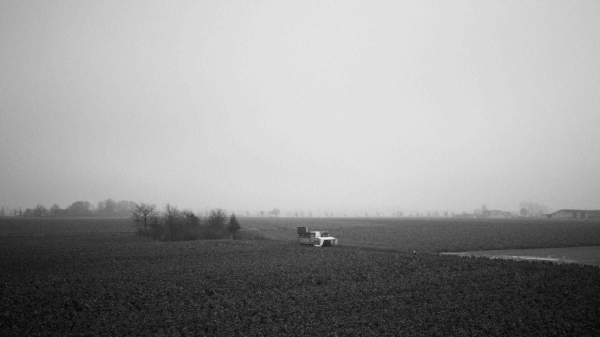 zwart-wit beeld van landbouwmachine op platteland, met boerderijen in achtergrond
