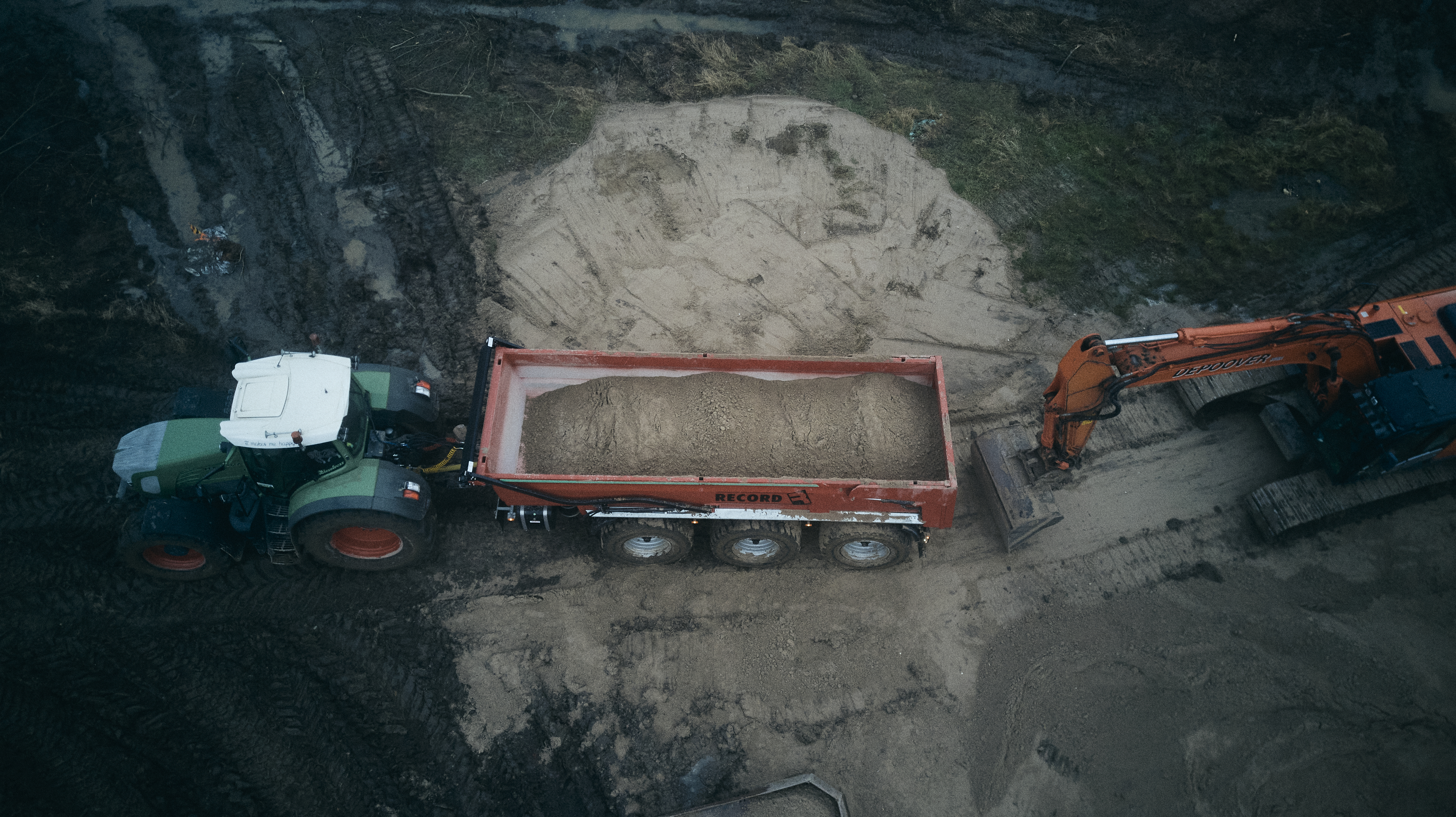 crane puts sand in hopper behind tractor
